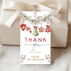 Pode incluir: Uma etiqueta de presente retangular com uma ilustração em aquarela de uma guirlanda festiva com enfeites de pão de mel pendurados em vermelho, verde e branco. O texto THANK YOU FOR COMING FROM THE BROWNS está em letras vermelhas, pretas e douradas.