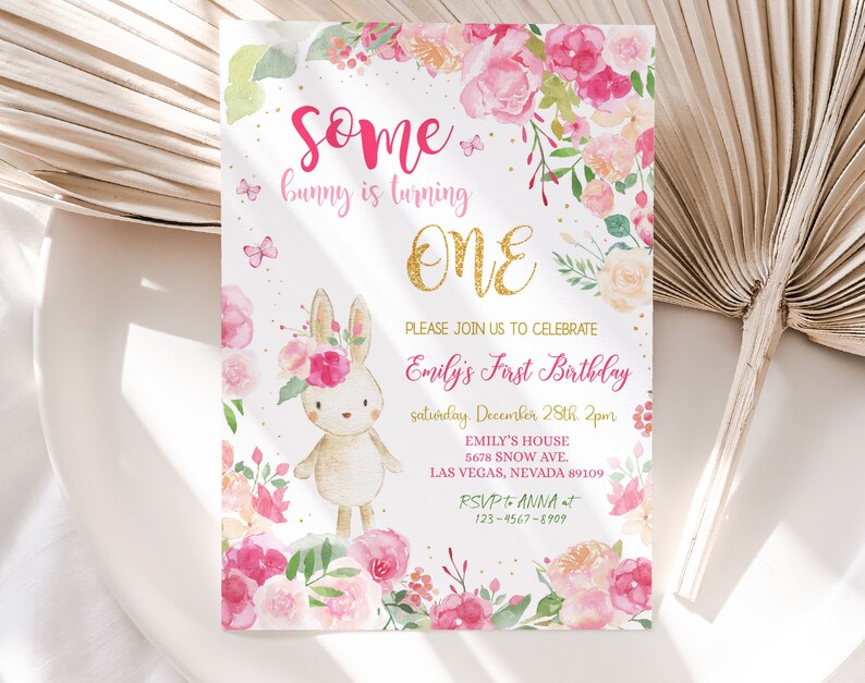 May include: A pink and gold first birthday invitation with a watercolor illustration of a bunny wearing a flower crown. The text reads "Some bunny is turning ONE. Please join us to celebrate Emily's First Birthday, Saturday, December 28th, 2pm. Emily's House, 5678 Snow Ave., Las Vegas, Nevada 89109. RSVP to Anna at 123-4567-8909."