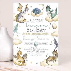 以下が含まれることがあります： 青と金の色の組み合わせのベビーシャワーの招待状。招待状には、水彩画で描かれたドラゴンと「A Little Dragon Is On His Way」というテキストが書かれています。