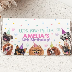 Puede incluir: Un envoltorio de chocolate blanco con un patrón de confeti colorido. Muestra una variedad de perros con sombreros de fiesta y el texto "Let's Paw-ty! It's Amelia's 4th Birthday!"