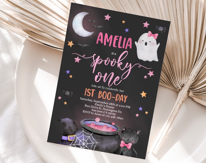 May include: A black and white invitation card with a pink and purple design. The card says "Amelia is a spooky one" and "1st Boo-Day". The card also features a ghost, a cauldron, and a black cat.