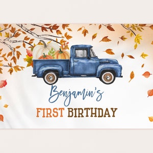 May include: A banner featuring a blue vintage truck carrying pumpkins, with autumn leaves and the text "Benjamin's FIRST BIRTHDAY." The banner is white with a watercolor style design and is strung with rope.