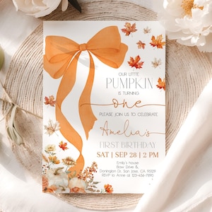 Puede incluir: Una invitación de cumpleaños con temática otoñal con un lazo naranja y hojas de otoño. El texto dice "Our Little Pumpkin is Turning One" e incluye el nombre "Amelia" y la fecha y hora de la fiesta.
