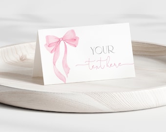 May include: A white folded card with a watercolor illustration of a pink bow and the text "YOUR text here". The card is displayed on a light-colored wooden tray.
