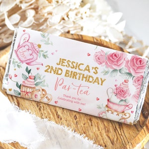 May include: Pink and gold chocolate bar wrapper with a tea party theme. The wrapper features a teapot, cupcakes, and roses. The text on the wrapper reads "Jessica's 2nd Birthday Par-tea Thank you for celebrating with me!"