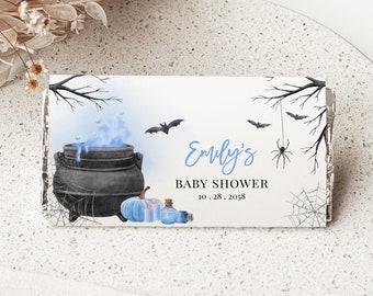May include: A white chocolate bar wrapper with a Halloween theme. The wrapper features a black cauldron with blue smoke, a spider's web, bats, and a pumpkin. The text on the wrapper reads "Emily's Baby Shower 10.28.2058".