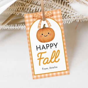 May include: A rectangular gift tag with a pumpkin illustration and the words "HAPPY Fall" in black and orange. The tag has a gingham pattern border and a bow at the top. The text "From, Amelia" is at the bottom.