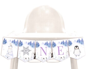 May include: A purple and white high chair banner with a winter theme. The banner features a polar bear, a snowflake, the letters "N" and "E", and a penguin. The banner is perfect for a first birthday party.