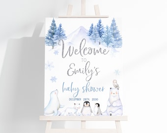 May include: A white sign featuring a winter landscape with blue pine trees and mountains. Text reads: Welcome to Emily's baby shower December 28th, 2030. Illustrations include a seal, arctic fox, two penguins, a polar bear, and an owl.