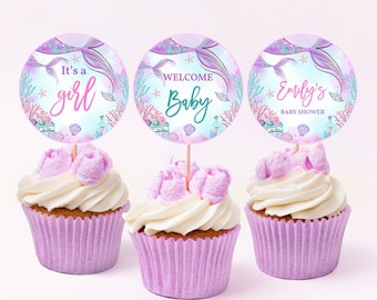May include: Three purple and blue cupcake toppers with mermaid tails, seashells, and starfish. The toppers say "It's a girl", "Welcome Baby", and "Emily's Baby Shower".