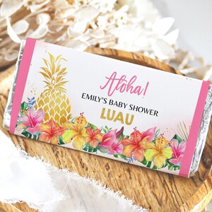 May include: A pink and white chocolate bar wrapper with a gold pineapple design and the text "Aloha! Emily's Baby Shower Luau".