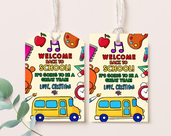 Puede incluir: Dos etiquetas de regalo amarillas y azules con el tema del autobús escolar con el texto "¡Bienvenido de vuelta a la escuela! ¡Va a ser un gran año! Con cariño, Cristina" sobre un fondo amarillo con útiles escolares coloridos.