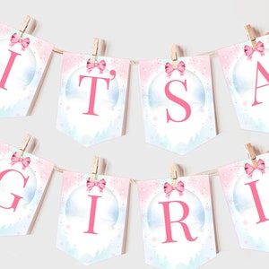 Puede incluir: Una pancarta rosa y azul con las palabras "It's a Girl" en letras rosas. Cada letra está en una bandera separada con un lazo rosa y un diseño de copo de nieve.