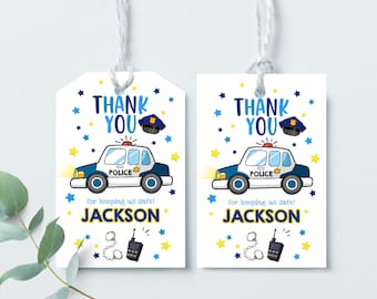 May include: Two blue and white thank you tags with a cartoon police car, a police hat, handcuffs, and a walkie talkie. The text on the tags reads "Thank You" and "for keeping us safe! Jackson".