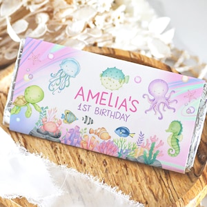 May include: A pink and blue chocolate bar wrapper with a seahorse, octopus, jellyfish, turtle, and fish. The wrapper says "Amelia's 1st Birthday".