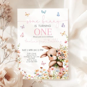 May include: A pink and white invitation card with a bunny rabbit holding flowers. The card says "some bunny is turning one" and has a floral design. The text also includes the date, time, and location of the event.