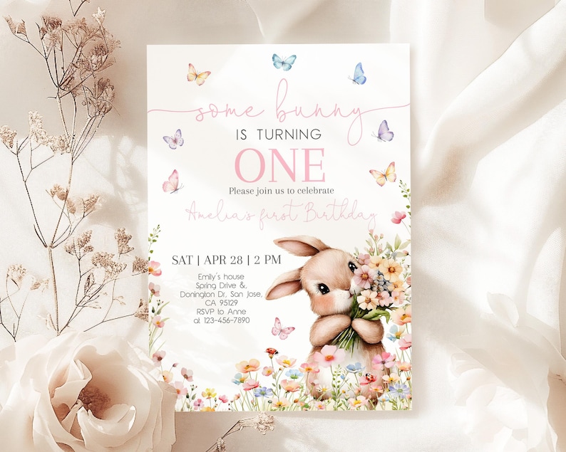 May include: A pink and white invitation card with a bunny rabbit holding flowers. The card says "some bunny is turning one" and has a floral design. The text also includes the date, time, and location of the event.