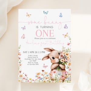 May include: A pink and white invitation card with a bunny rabbit holding flowers. The card says "some bunny is turning one" and "Amelia's first birthday". The invitation includes the date, time, and location of the party.