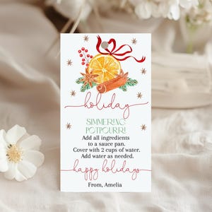 Op de afbeelding: Een witte kaart met een aquarel illustratie van een sinaasappelschijf, kaneelstokje en steranijs, met de woorden "holiday simmering potpourri" in rood script. De kaart bevat instructies en de woorden "happy holidays."