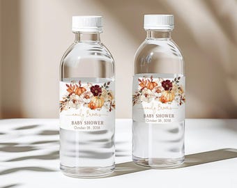 May include: Two clear water bottles with white caps. Each bottle has a label featuring a floral design with pumpkins and the text "emily Brooks BABY SHOWER October 28, 2058". The bottles are on a white surface.