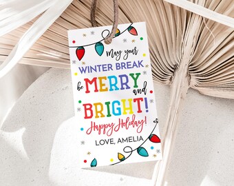 May include: A white gift tag with a brown string, featuring colorful text that reads "May your WINTER BREAK be MERRY and BRIGHT! Happy Holiday! LOVE, AMELIA." The tag is decorated with string lights.