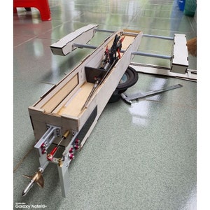 Puede incluir: Un modelo de barco de madera con una hélice y un motor. El barco está desmontado y las piezas están dispuestas en un suelo de baldosas.