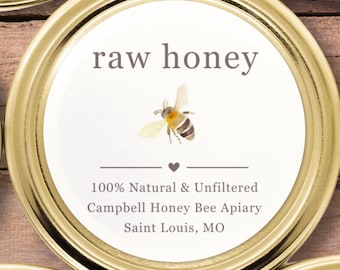 May include: A round gold metal jar lid featuring a white label with the text raw honey, a small bee illustration, a heart icon, and the text 100% Natural & Unfiltered, Campbell Honey Bee Apiary, Saint Louis, MO printed in dark grey lettering.