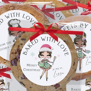 May include: Close-up of several large chocolate chip cookies, each individually wrapped and tied with a red ribbon. The cookies have circular labels that read "Baked with Love" and "Merry Christmas!" with a cartoon chef illustration.