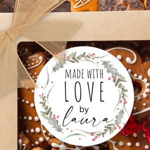 May include: A white round sticker with a green and red watercolor wreath design. The sticker says "Made with Love by Laura".