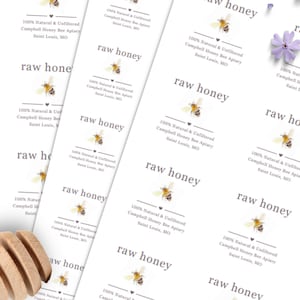 May include: White rectangular labels with the text "raw honey" and "100% Natural & Unfiltered Campbell Honey Bee Apiary Saint Louis, MO". Each label features a bee illustration. A wooden honey dipper is visible.