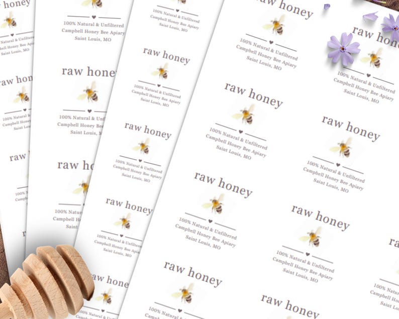 May include: White rectangular labels with the text "raw honey" and "100% Natural & Unfiltered Campbell Honey Bee Apiary Saint Louis, MO". Each label features a bee illustration. A wooden honey dipper is visible.