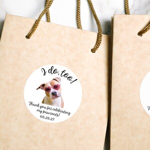 Puede incluir: Bolsas de regalo de papel marr&oacute;n claro con asas trenzadas, cada una con una pegatina blanca circular. La pegatina muestra un perro con gafas de sol rosas en forma de coraz&oacute;n con el texto: I do, too! Thank you for celebrating my pawrents! 05.25.27.