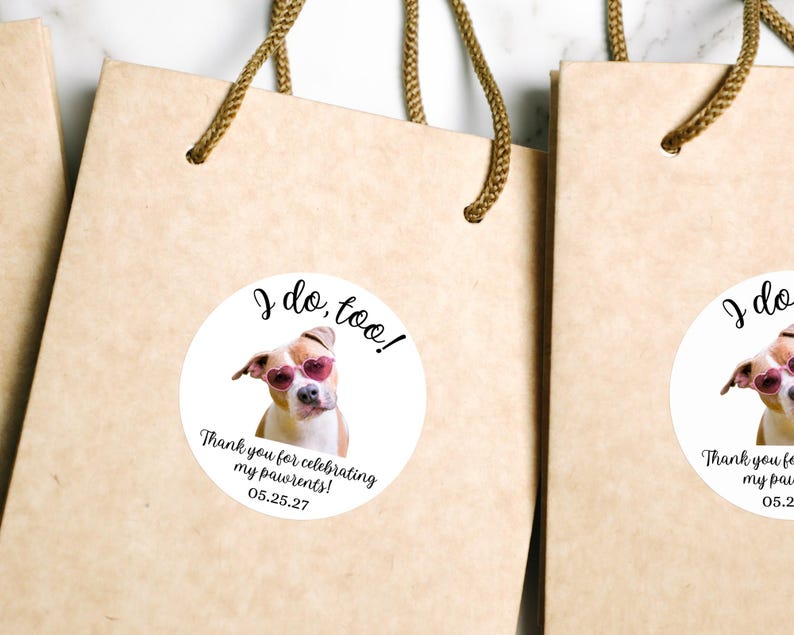 Puede incluir: Bolsas de regalo de papel marr&oacute;n claro con asas trenzadas, cada una con una pegatina blanca circular. La pegatina muestra un perro con gafas de sol rosas en forma de coraz&oacute;n con el texto: I do, too! Thank you for celebrating my pawrents! 05.25.27.