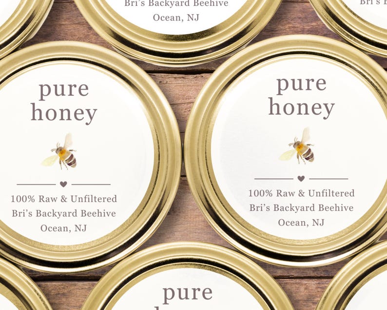 May include: Close-up of several golden jar lids with white labels. The labels read "pure honey" with a bee illustration. Text below states "100% Raw & Unfiltered" and the name and location of the beekeeper.