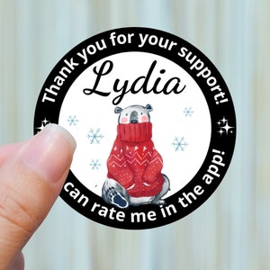 May include: A round sticker with a polar bear wearing a red sweater. The sticker has the text "Thank you for your support! Lydia can rate me in the app!" in a black border with snowflakes and stars.