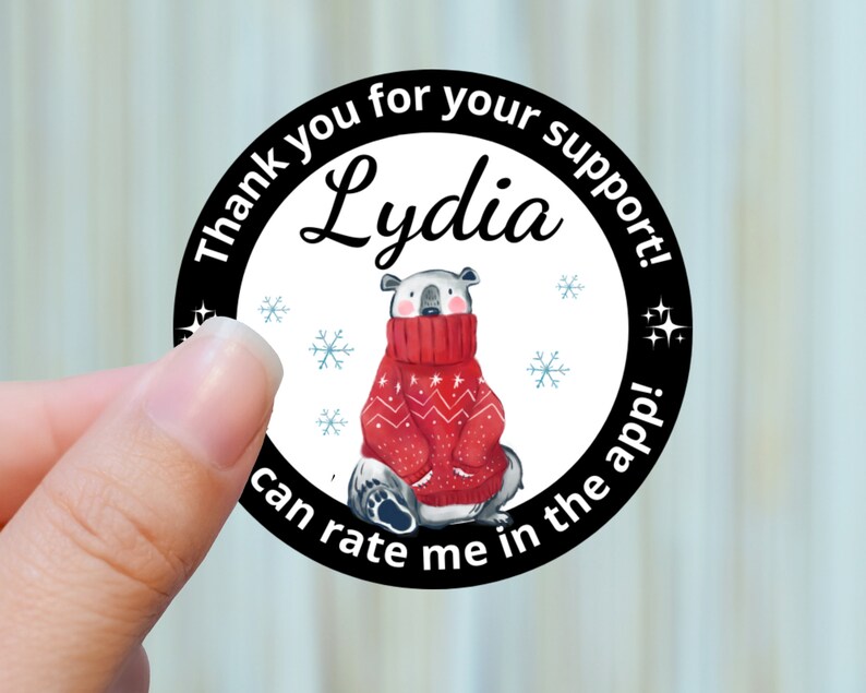 May include: A round sticker with a polar bear wearing a red sweater. The sticker has the text "Thank you for your support! Lydia can rate me in the app!" in a black border with snowflakes and stars.