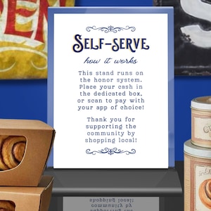Op de afbeelding: Een blauw omrand bord met de woorden "SELF-SERVE" en "how it works" in blauw script. Het bord legt het eerlijkheidssysteem voor betaling uit, met opties voor contant geld of betaling via een app. Kaneelbroodjes en andere bakwaren zijn zichtbaar.