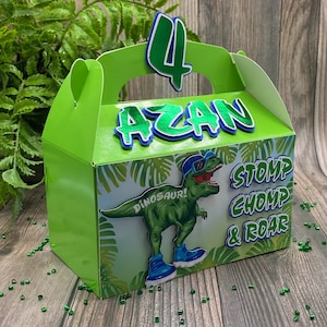 May include: Green and blue dinosaur party favor box with a dinosaur wearing sunglasses and the text "Dino-saur! Stomp, Chomp & Roar". The box also has the name "Azan" and the number "4" on it.