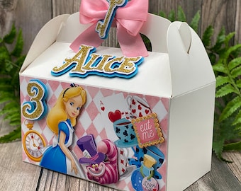 May include: White favor box with a pink bow and a gold key. The box has a pink and white checkered pattern with a picture of Alice in Wonderland, the Mad Hatter, and a teacup. The box says "Alice" and "Eat Me".