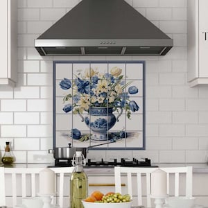 May include: A white kitchen with a white tiled backsplash and a stainless steel range hood. A blue and white ceramic tile with a floral design is mounted on the backsplash. The tile features a bouquet of blue and yellow flowers in a blue and white vase. The tile is labeled "Tempera Ceramic".