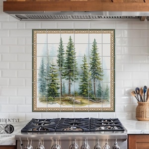 Puede incluir: Un salpicadero de cocina con un diseño de azulejos verde y marrón que presenta una pintura de acuarela de cinco pinos en un bosque brumoso. El diseño de los azulejos está enmarcado con un borde dorado y verde. El salpicadero está sobre una estufa de acero inoxidable con una rejilla de quemador negra.