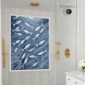 May include: A white bathroom with a shower stall featuring a blue and white tile mural of fish swimming. The shower stall has a gold shower head and a gold shower handle. There is a white vanity with gold handles and a gold mirror with a gold frame.