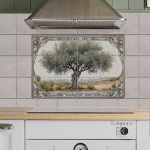 Op de afbeelding: Een keukenachterwand met een decoratieve tegel met een handgeschilderde olijfboom met een gedetailleerd, ingewikkeld frame. De tegel is gemaakt door Tempera Ceramic.