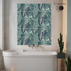 Op de afbeelding: Een badkamer met een witte badkuip en een muur bedekt met keramische tegels. De tegels tonen een herhalend patroon van teal en donkergroene tropische bladeren. De merknaam "Tempera Ceramic" is rechtsboven zichtbaar.