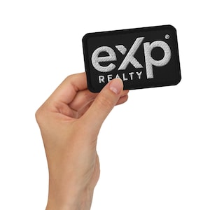 Può includere: Una toppa rettangolare nera con la scritta ricamata "exp REALTY" in bianco. La toppa è tenuta in mano su sfondo bianco. La toppa ha un bordo nero.