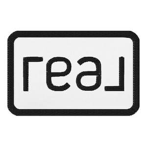 May include: White rectangular patch with a black border and the word "real" in black lettering.