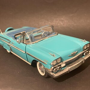 May include: A turquoise convertible car model with a blue interior and white-walled tyres. The classic car has chrome detailing on the front grill, bumpers, and side trim. The model has a spare tyre on the back.