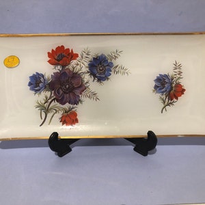 May include: Rectangular white glass serving tray with a gold rim and floral design. The flowers are in shades of red, blue, and purple. A small gold sticker is on the left side of the tray.