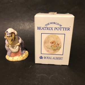 May include: A small porcelain figurine of a mouse wearing a purple dress and a white apron. The figurine is part of a collection called "The World of Beatrix Potter" by Royal Albert.