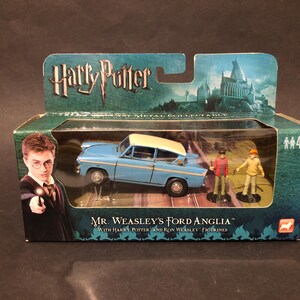 May include: A boxed toy set featuring Mr. Weasley's Ford Anglia, a light blue car with a cream roof, and Harry Potter and Ron Weasley figurines. The box has the Harry Potter logo and a picture of Hogwarts.